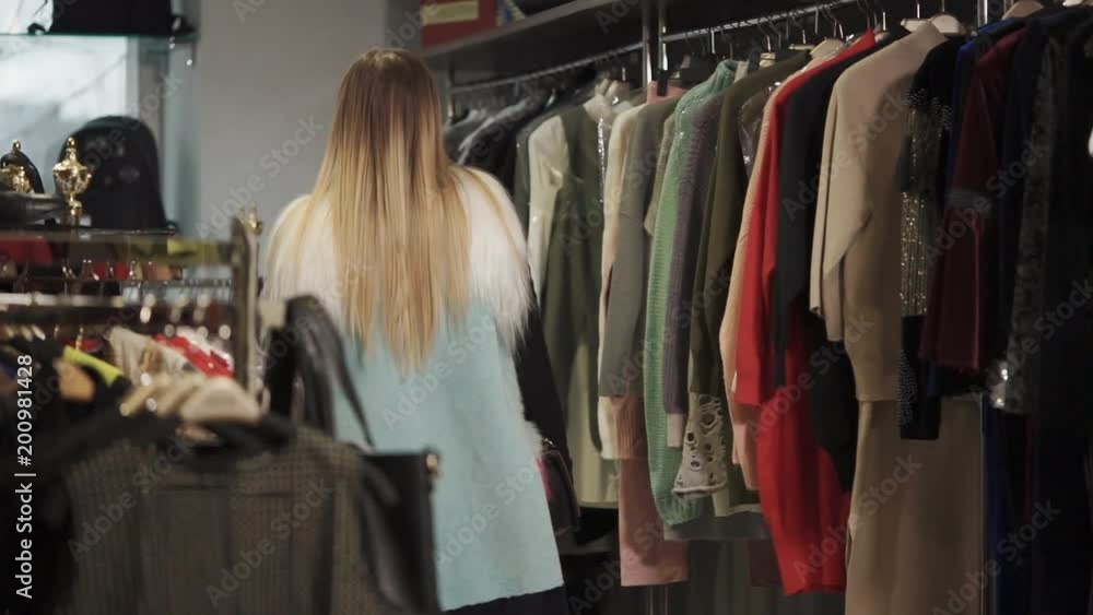 Slim young woman is strolling in a clothes shop. She is looking on hangers and deciding to buy, consumer behavior and merchandising Slim young woman is strolling in a clothes shop. She is looking on hangers and deciding to buy, consumer behavior and merchandising