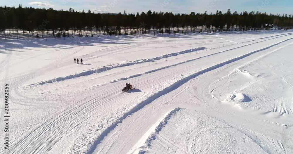 Snowmobile, C4k aerial view following a skidoo, driving over a frozen lake, near sallatunturi mountain fell, on a sunny winter day, in Salla, Lapland, Finland Snowmobile, C4k aerial view following a skidoo, driving over a frozen lake, near sallatunturi mountain fell, on a sunny winter day, in Salla, Lapland, Finland