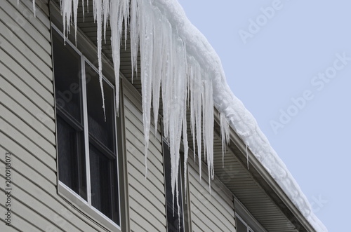 Close up of a house with snow covered roof and long icicles hanging from the eaves-through and gutter