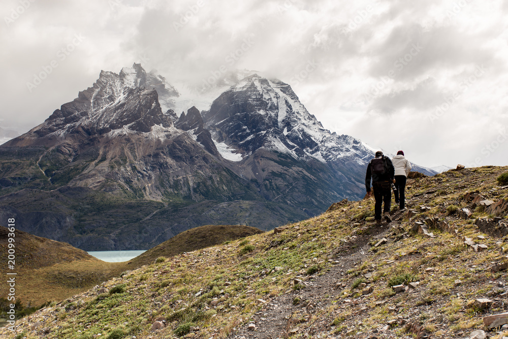 hikers dressed in dark clothing walking along pathway with Torres del Paine mountain range in the back