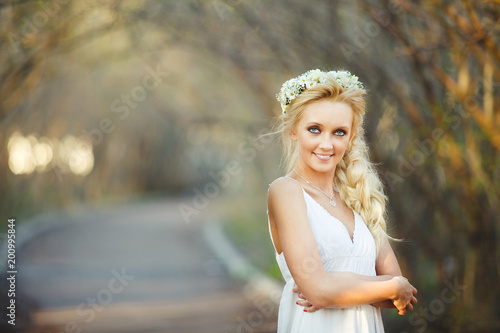 beautiful blond woman in white dress and floral wreath on her head. cute person in alley.
