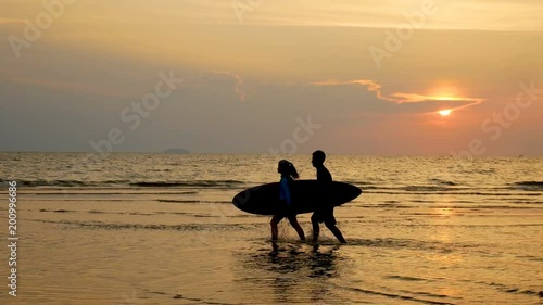 4K. silhouette of young happy surf man and woman running with long surf boards at sunset on tropical beach. surfer on the beach in sea shore at sunset time with beautiful light. 