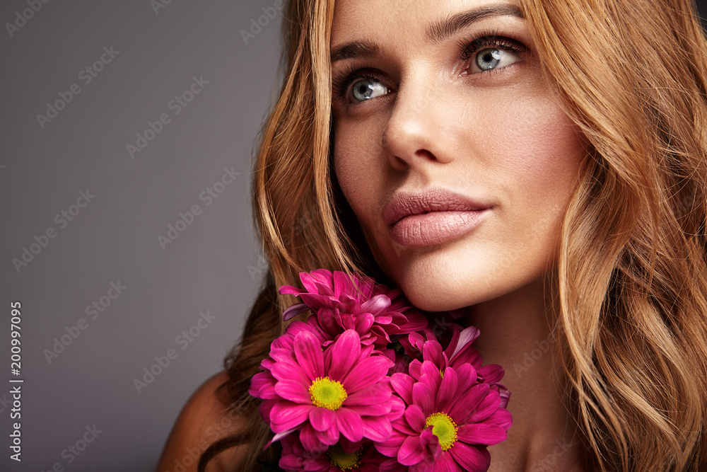 Beauty fashion portrait of young blond woman model with natural makeup and perfect skin with bright сrimson chrysanthemum flower posing in studio Beauty fashion portrait of young blond woman model with natural makeup and perfect skin with bright сrimson chrysanthemum flower posing in studio