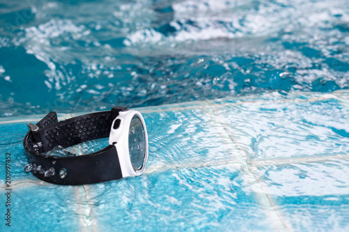 Waterproof digital wristwatch placed on the edge of the swimming pool.