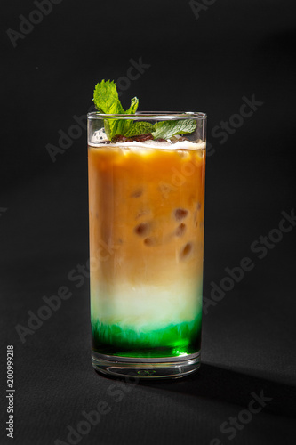 A multicolored, three-layered opaque cocktail in a tall glass with crushed ice and mint leaves and coffee beans, with the taste of menthol, coffee, caramel, cream. Side view. Isolated black background
