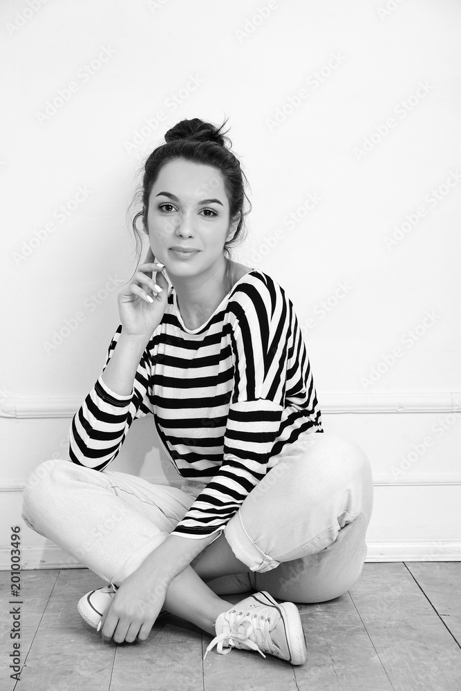 Fototapeta premium Portrait of young beautiful brunette woman girl model with nude makeup in summer hipster clothes posing near wall. Sitting on the floor