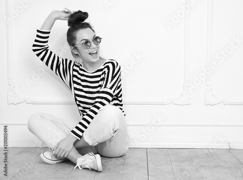 Portrait of young beautiful brunette woman girl model with nude makeup in summer hipster clothes posing near wall in sunglasses. Sitting on the floor