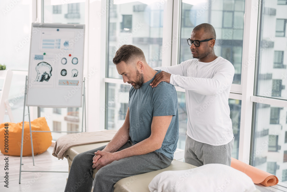 Muscle relaxation. Smart nice man standing behind his patient while doing a shoulder massage Muscle relaxation. Smart nice man standing behind his patient while doing a shoulder massage