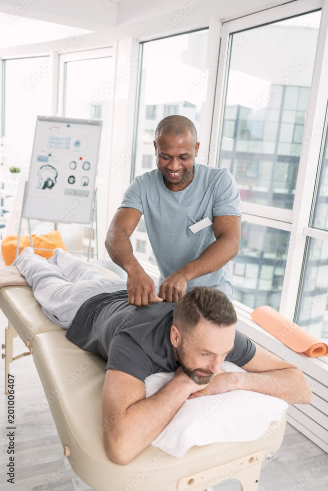 Massage therapy. Pleasant cheerful man having a massage while visiting a rehabilitation center Massage therapy. Pleasant cheerful man having a massage while visiting a rehabilitation center