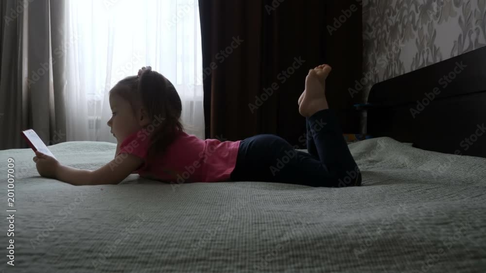 A cute little girl is playing with a smartphone, watching a video in the phone. Children and gadgets. A cute little girl is playing with a smartphone, watching a video in the phone. Children and gadgets.
