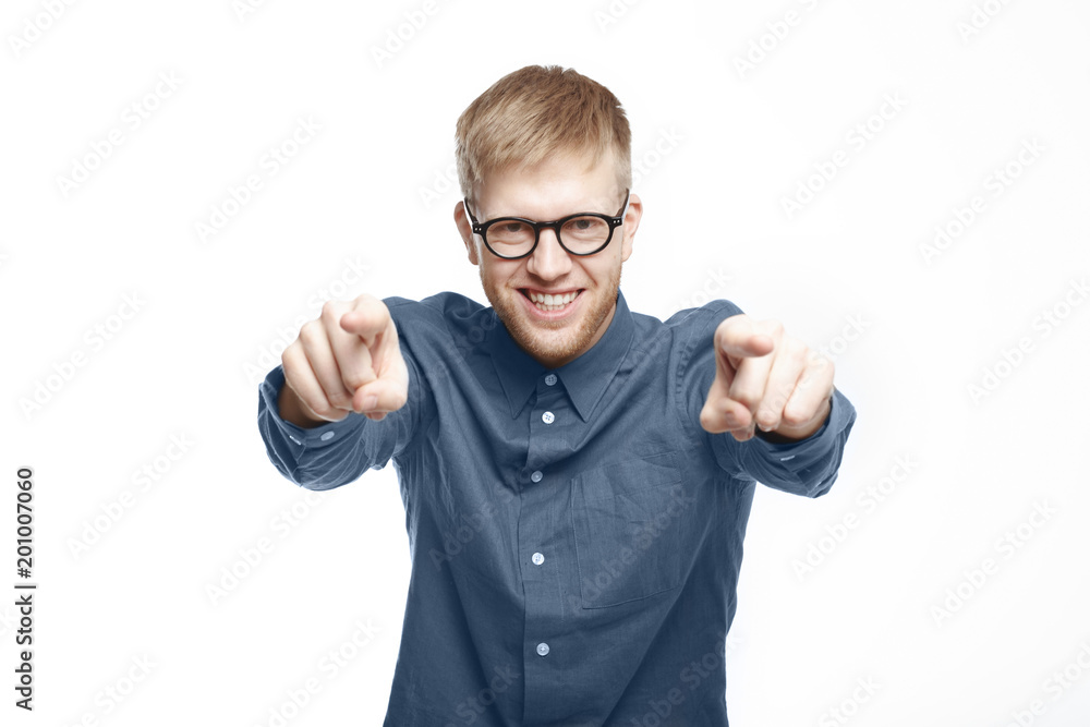 It's your chance. Handsome confident young unshaven male in stylish eyeglasses and brown shirt pointing index fingers at camera, choosing you, smiling excitedly, posing against white wall background It's your chance. Handsome confident young unshaven male in stylish eyeglasses and brown shirt pointing index fingers at camera, choosing you, smiling excitedly, posing against white wall background