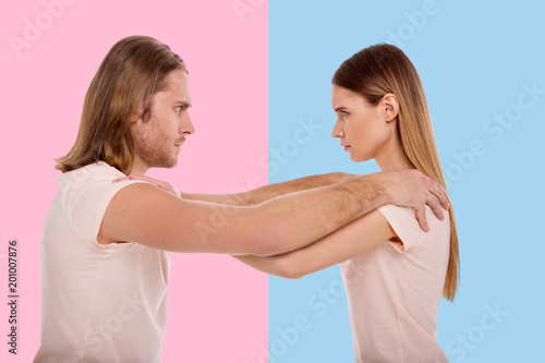Equal power. Serious focused man and woman having a hold of each others shoulders and staring at each other intensely while standing against blue and pink background