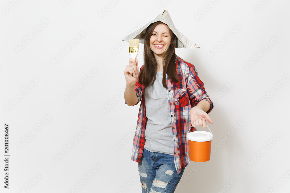 Young overjoyed beautiful woman in newspaper hat blinking and holding paint brush and paint bucket isolated on white background. Instruments, tools for renovation apartment room. Repair home concept. Young overjoyed beautiful woman in newspaper hat blinking and holding paint brush and paint bucket isolated on white background. Instruments, tools for renovation apartment room. Repair home concept.