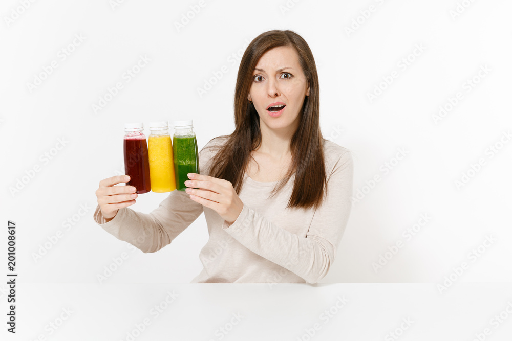 Young woman at table with green, red and yellow detox smoothies in bottles isolated on white background. Proper nutrition, vegetarian drink, healthy lifestyle, dieting concept. Area with copy space. Young woman at table with green, red and yellow detox smoothies in bottles isolated on white background. Proper nutrition, vegetarian drink, healthy lifestyle, dieting concept. Area with copy space.