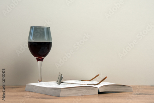 Still life. Glass of red wine with open book and reading glasses.