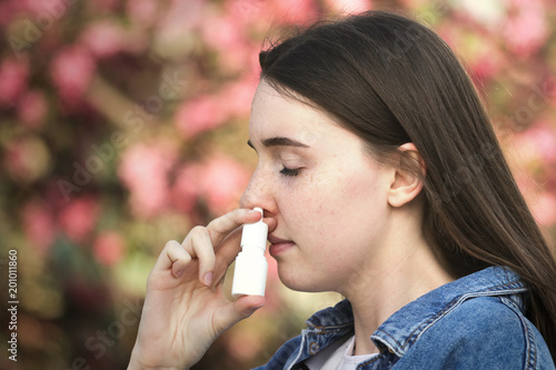 Teenager girl using nose inhaler in park over pink flower