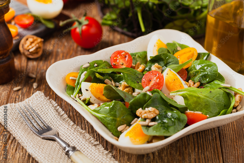 Delicious salad of fresh spinach, boiled egg, tomatoes, nuts and sunflower seeds Delicious salad of fresh spinach, boiled egg, tomatoes, nuts and sunflower seeds