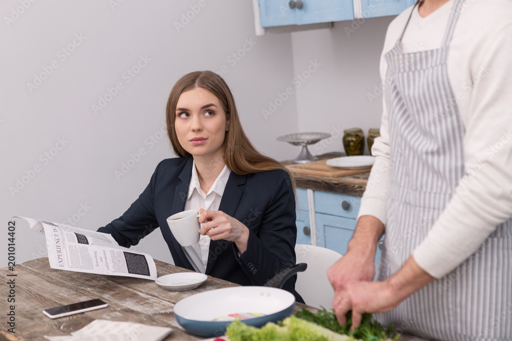I love coffee. Cheerful dominant woman drinking coffee while her boyfriend cooking I love coffee. Cheerful dominant woman drinking coffee while her boyfriend cooking