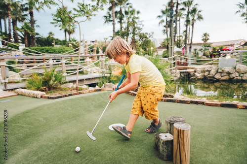 Funny kid boy playing mini golf, child enjoying summer vacation