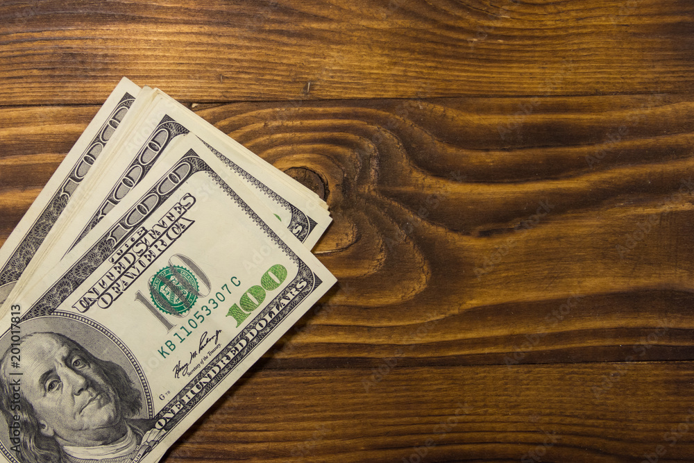 One hundred dollars bills on wooden desk One hundred dollars bills on wooden desk