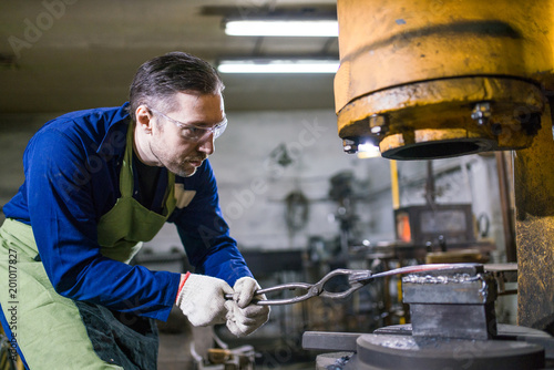 The smith works with an electric hammer.