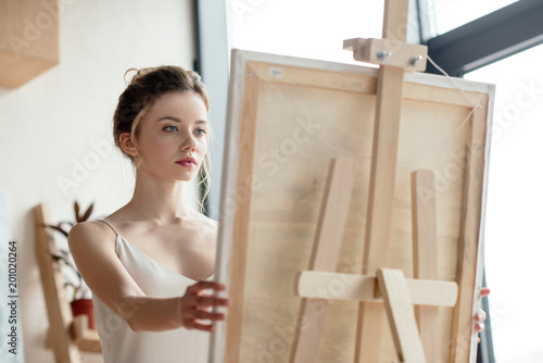 beautiful young artist looking at picture on easel