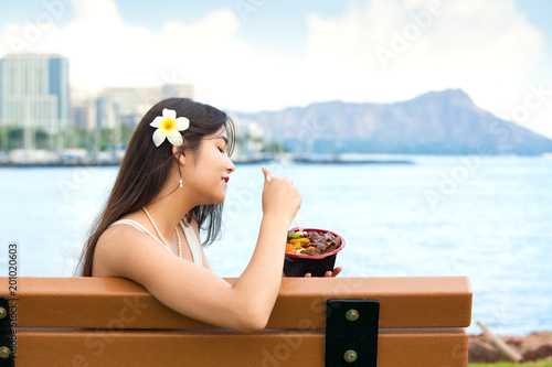 Young woman eating Hawaiian bqq beef on bench in Hawaii photo