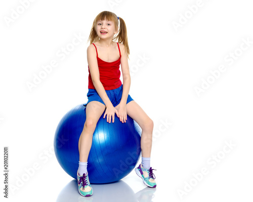 A little girl is jumping on the big gym ball.