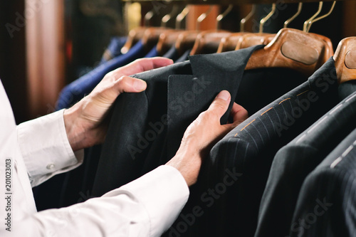 A handsome man with a white shirt  is choosing a jacket from the clothes hangers