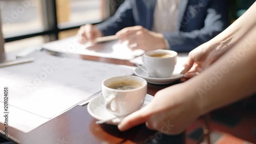 Close up of waitress hands putting two cups of coffee to the table in front of architect working on house blueprint. Concept: architecture, blueprint house, paper work