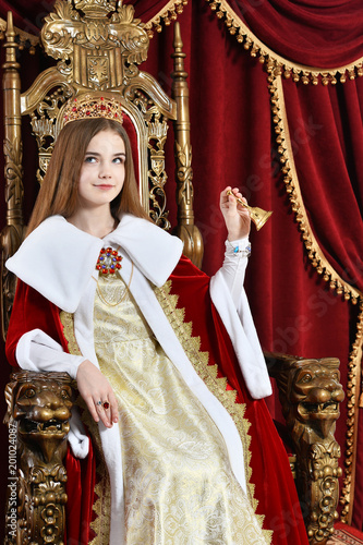 Beautiful teen girl with crown holding hand bell while sitting