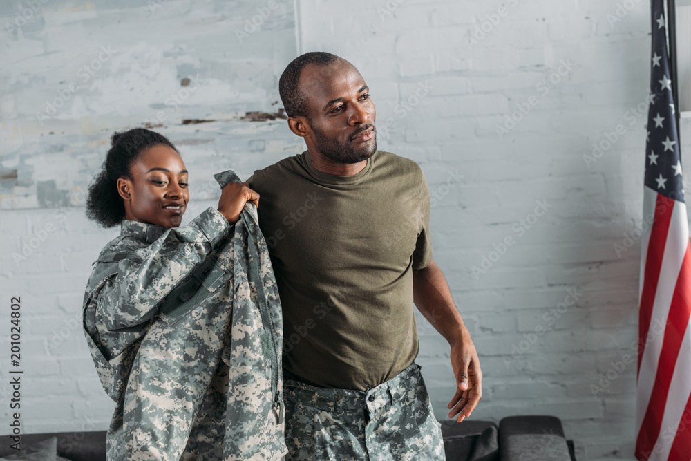 African american female soldier helping man to get dressed in camouflage clothes