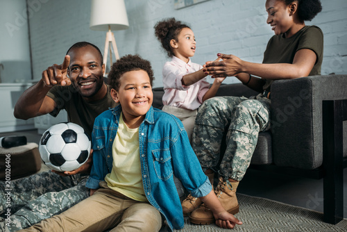 African american female and male soldiers playing with their children at home