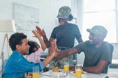 Parents in camouflage clothes giving five to their children by kitchen table