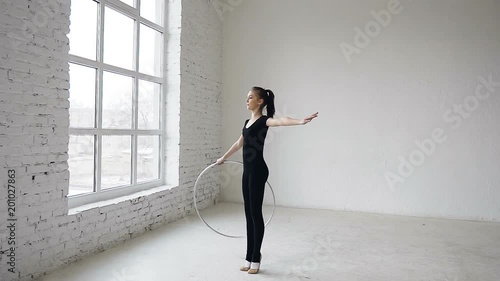 Young attractive girl in black body training a gymnastics exercise with a hoop in the sports school at white background photo