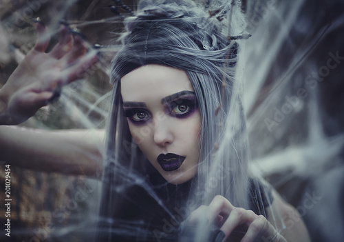 Beautiful sexy Gothic girl with pale skin and long white hair like spider black widow in spider web. Dark Princess with long vampire claws in the crown. Spider woman weaving net. Gothic look.