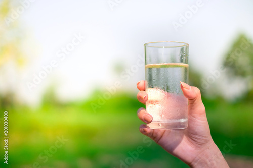 Woman hand holds a glass of cold water on outdoors background with copy space.