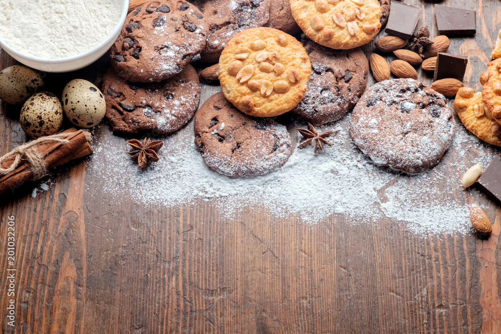 Chocolate chips cookies, peanut cookies and scattered nuts on old dark rustic texture with copy space for your text. Top view. Chocolate chips cookies, peanut cookies and scattered nuts on old dark rustic texture with copy space for your text. Top view.