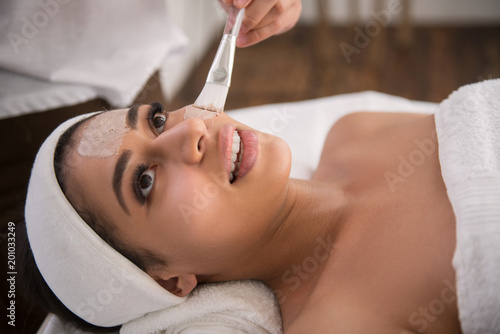 Pleasant feeling. Cheerful nice woman being in a good mood while having her facial mask applied on the face