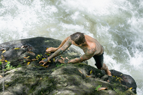 overhead view of tattooed man climbing on rocks with river on background, Bali, Indonesia