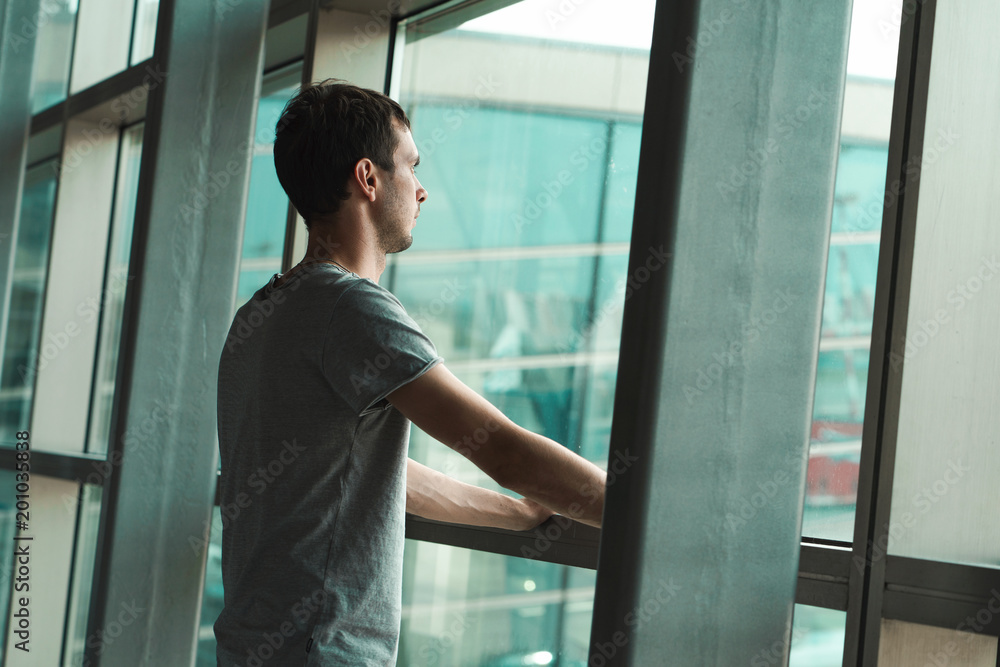 Young man is waiting for his flight and loooking at the window Young man is waiting for his flight and loooking at the window