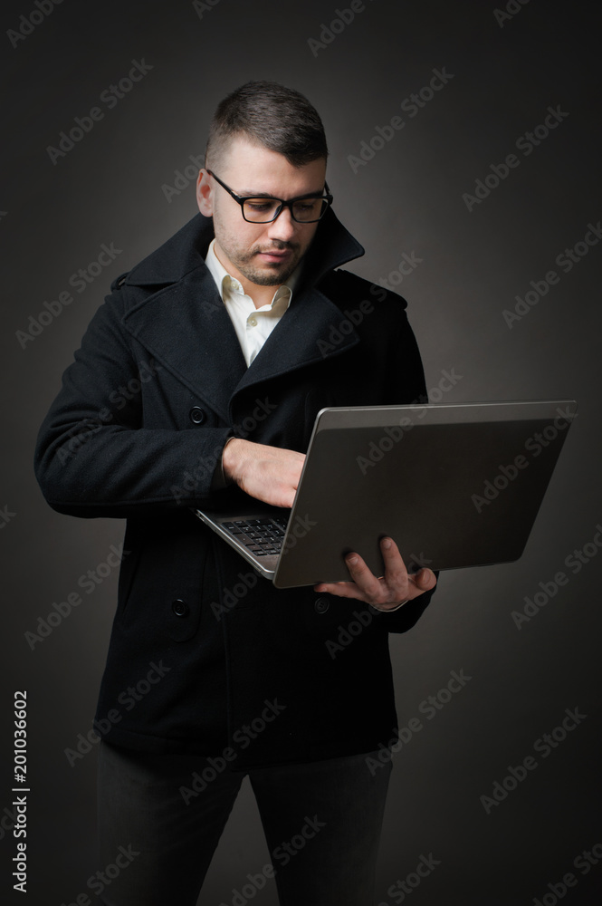 business man in classic jacket and glass holding laptop on dark background. business man in classic jacket and glass holding laptop on dark background.
