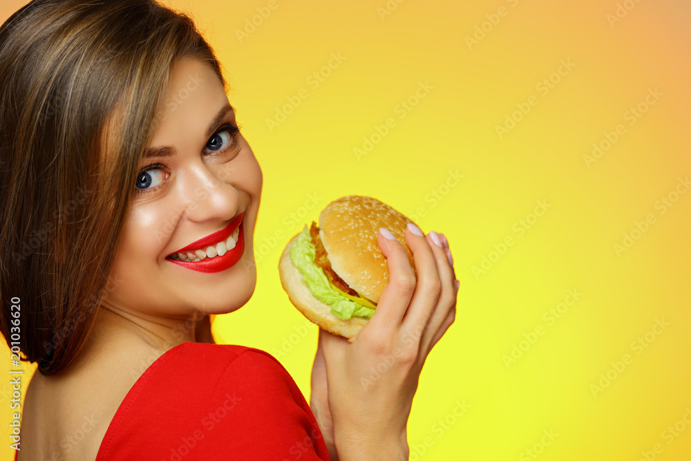 Smiling girl holding burger looks over shoulder. Smiling girl holding burger looks over shoulder.