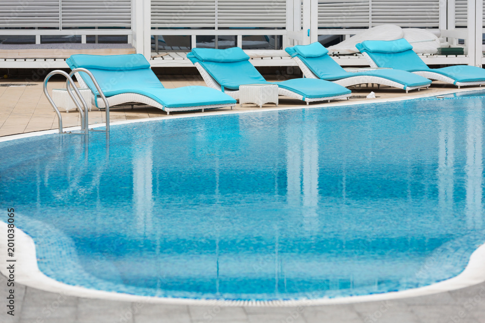 four wide turquoise deck chairs are beside the pool, reflected in the water, concept travel, vacation