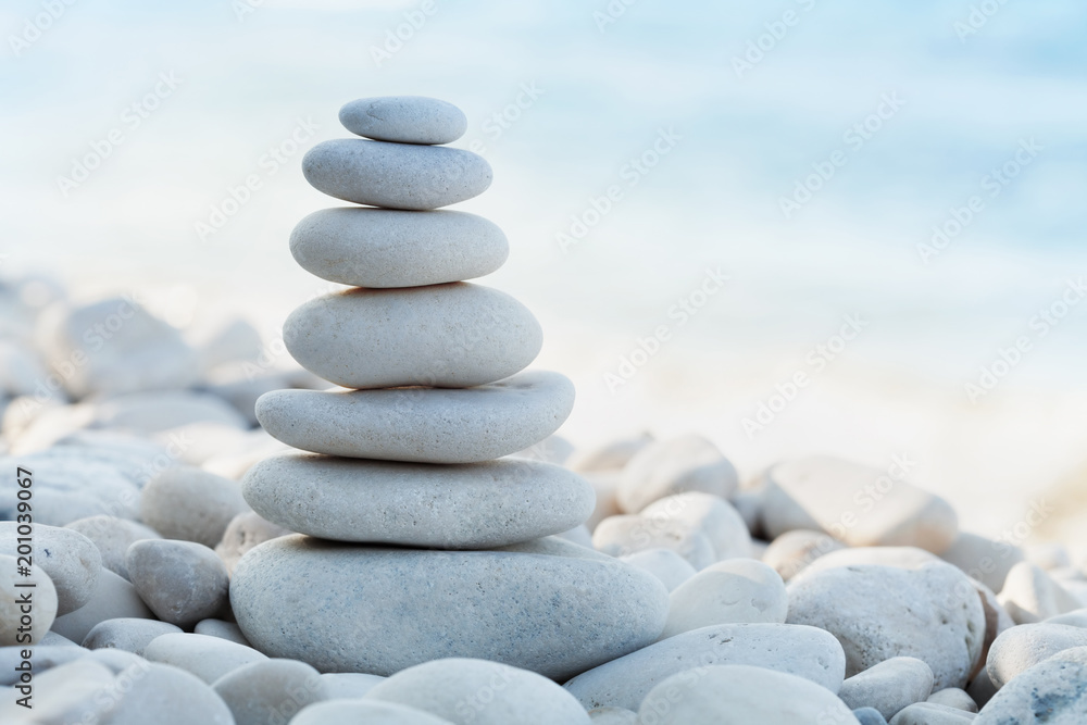 Stack of white pebbles stone against sea background for spa, balance, meditation and zen theme. - obrazy, fototapety, plakaty 