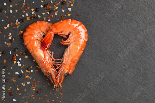 Two big prawns /shrimps heart shape with spices and seasoning on black stone plate with copy space. photo