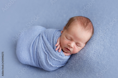 Photoshoot of a sleeping newborn boy on a blue background, wrapped in peanuts