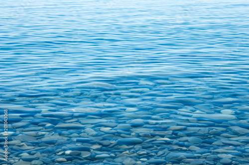 The texture of the water. Clear blue sea water with a large and small stones on the bottom, near the shore