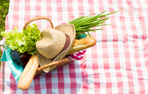 Picnic backet full of food and drinks on checkered tablecloth, top view