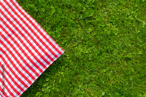 Green grass and checkered tablecloth background for picnic, top view